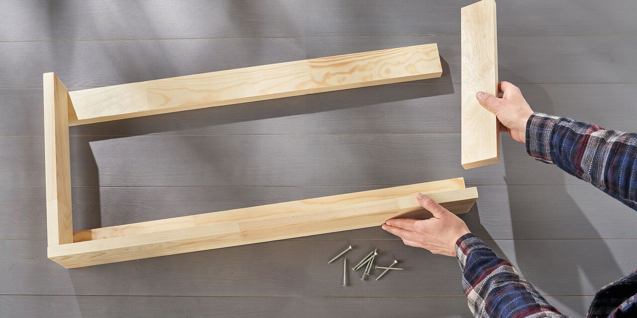 Eine Person mit Holzstücken und Schrauben, die ein Möbelstück zusammenbauen.