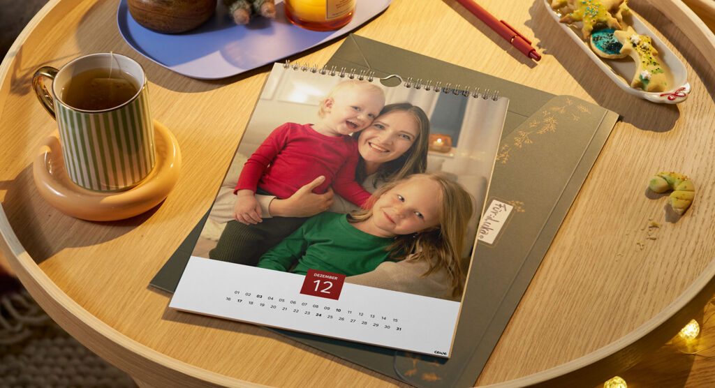 Kalender mit Familienfotos auf einem Tisch mit Weihnachtsdekoration. Dahinter eine Geschenkverpackung.