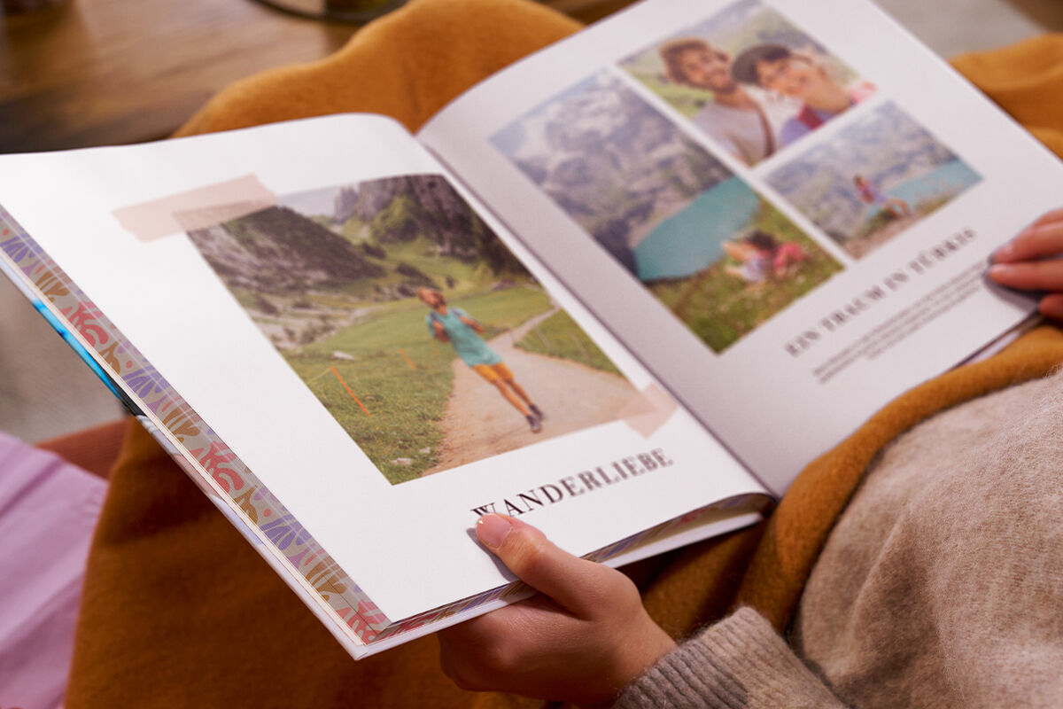 Eine Frau sitzt auf einem Sofa und blättert durch ein CEWE FOTOBUCH, das auf ihrem Schoß liegt.